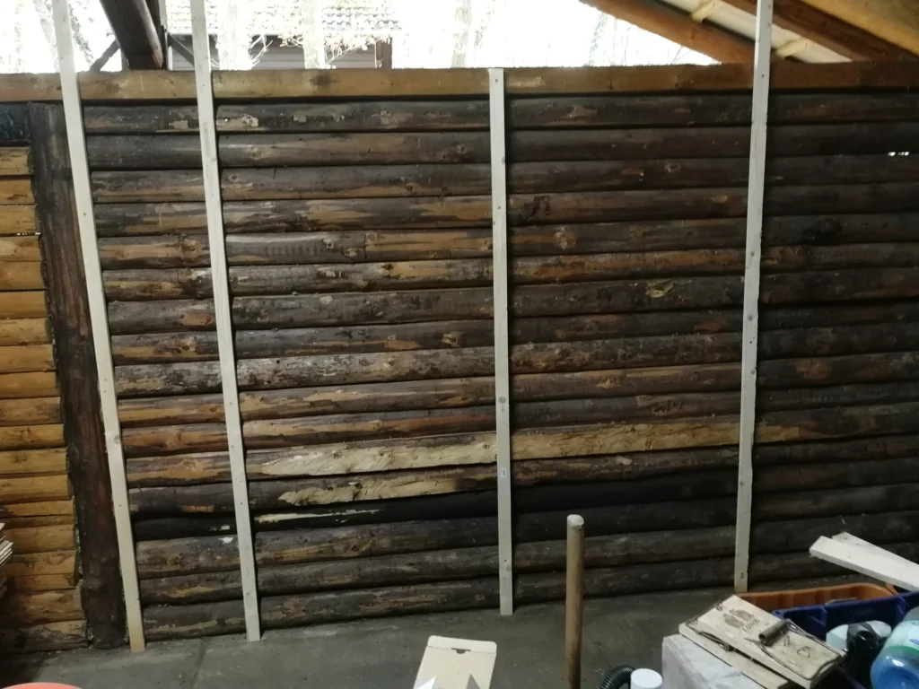 Wand aus Holzstämmen mit senkrechten Dachlatten