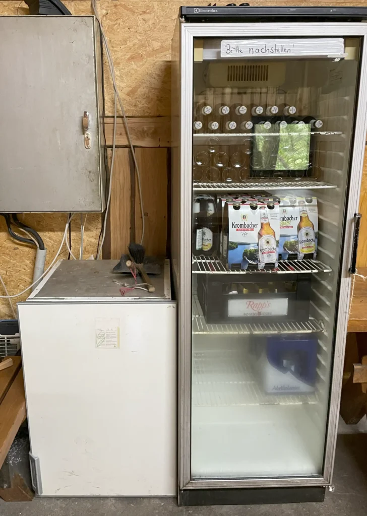 Bild zwei nebeneinander stehenden Kühlschränke, der rechte Kühlschrank ist kleiner als der rechte Kühlschrank. Im rechten Kühlschrank liegen hinter der Glastür Getränkeflaschen.