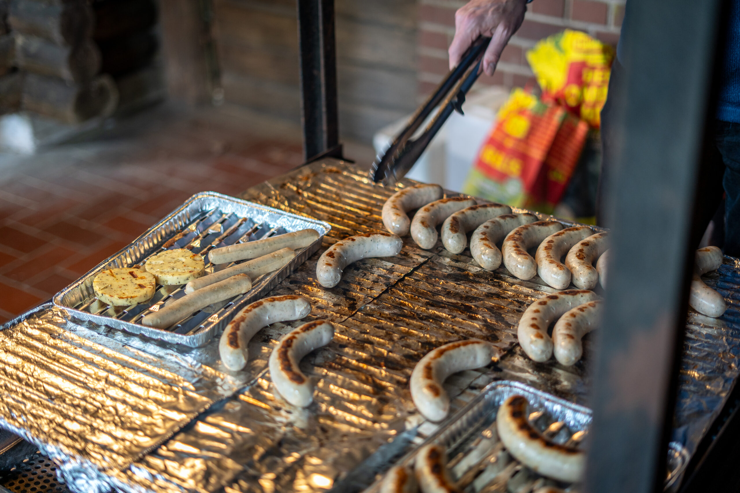 Würstchen auf einem Grill, eine Grillzange ragt in das Bild